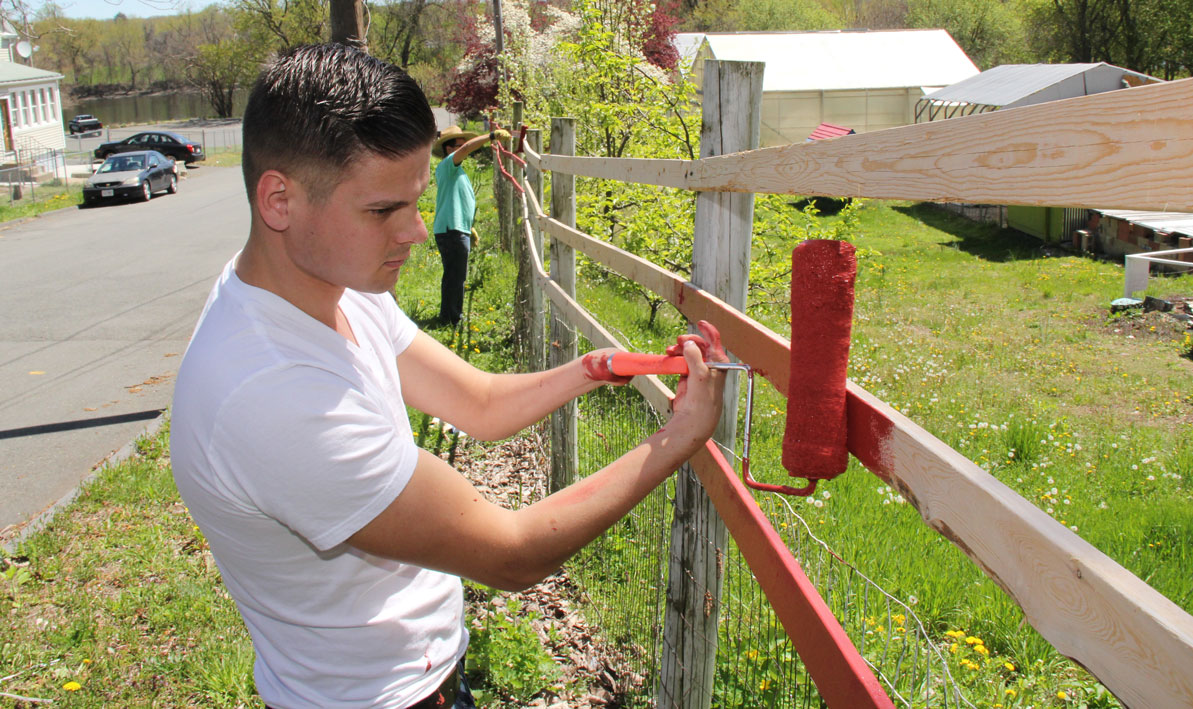 HCC student paints fence at Nuestras Raices farm in Holyoke during a volunteer day last spring.