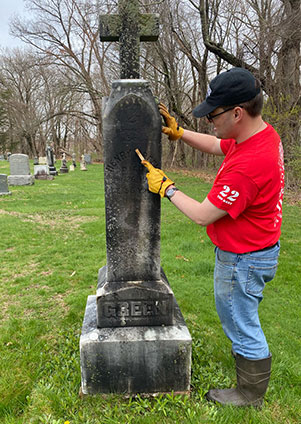Camo club member cleans a grave marker in Easthampton
