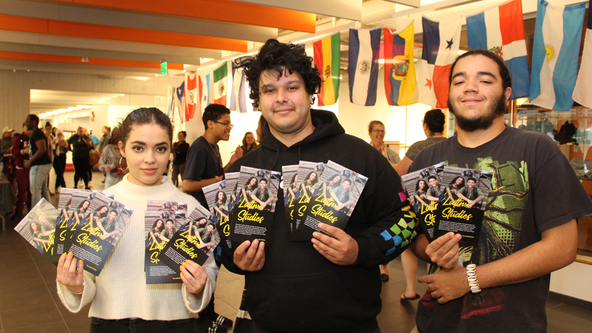 Three HCC students pose holding Latinx Studies brochures
