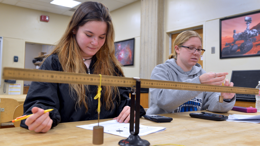 Two physics students work with a ruler and weights