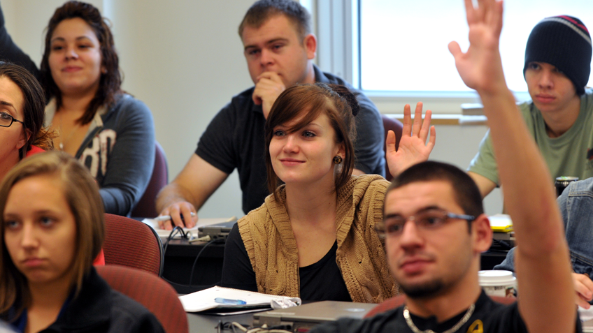 A classroom of students raising their hands and smiling