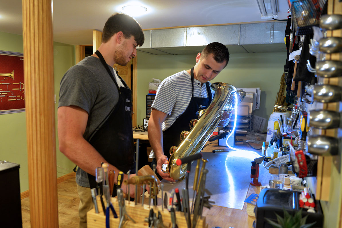 David '17 and Roman '17 work on a baritone saxophone in their basement workshop.  