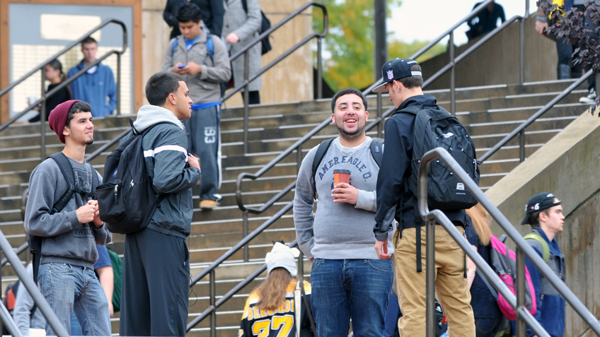 A group of male students talking outside on the campus of holyoke community college