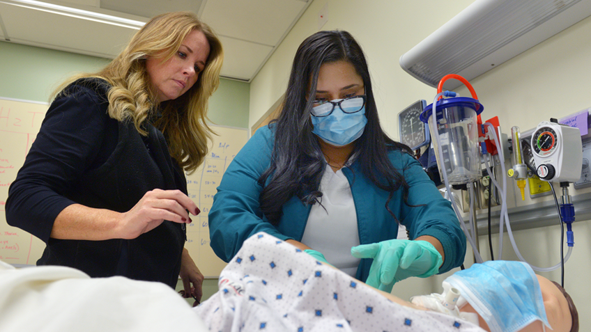 A healthcare student works on a patient simulator while an instructor looks on