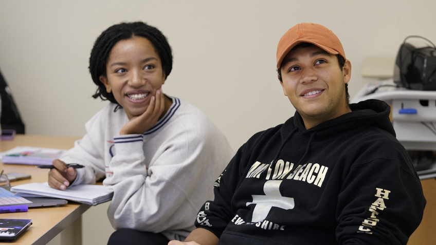 Two students are seated in a classroom smiling