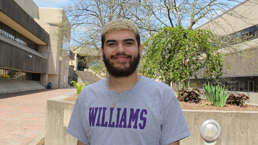 Armanis Fuentes is wearing a Williams College tshirt and standing outside on the campus of Holyoke Community College