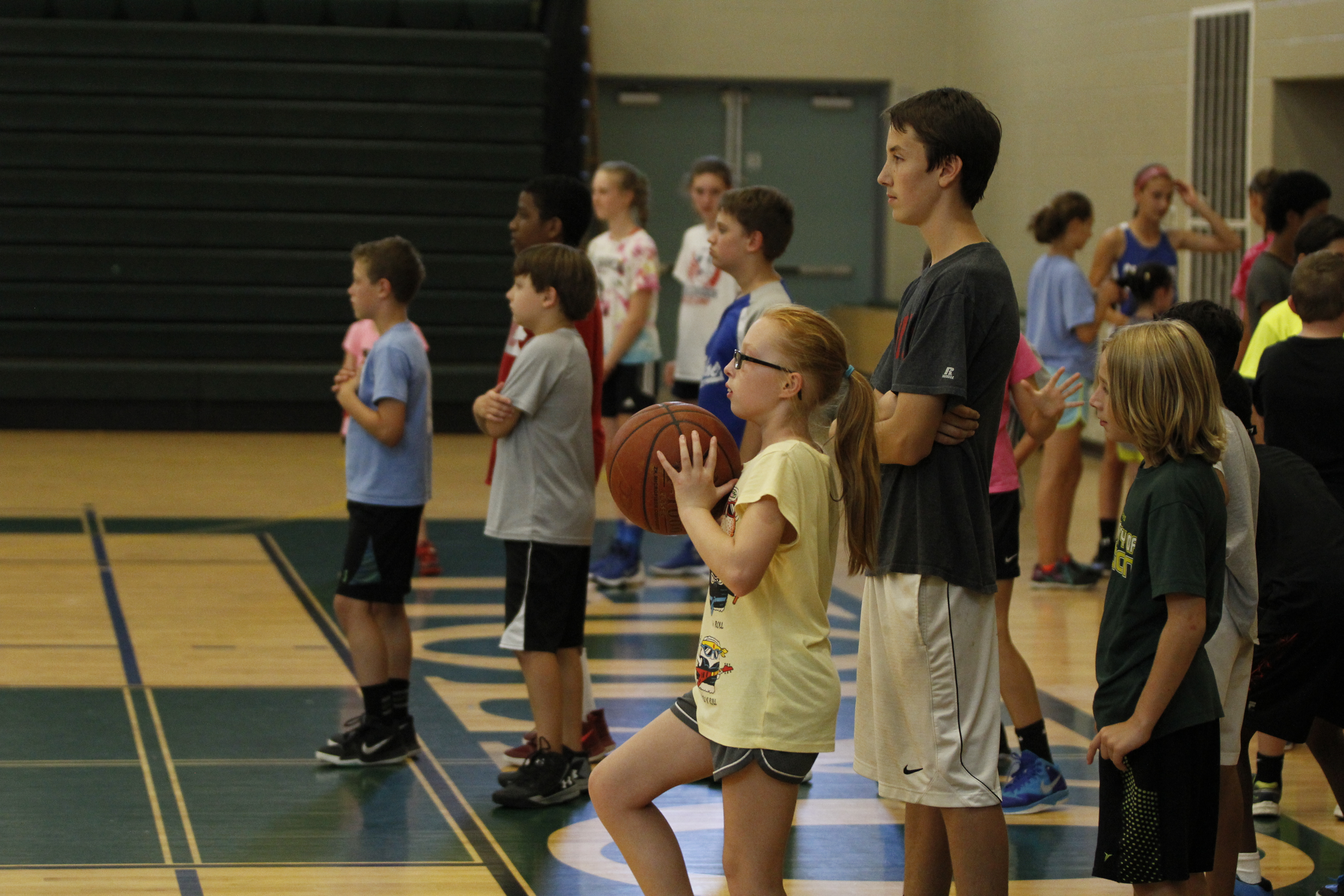 A group of children stand in a gymnasium. One holds a basketball.