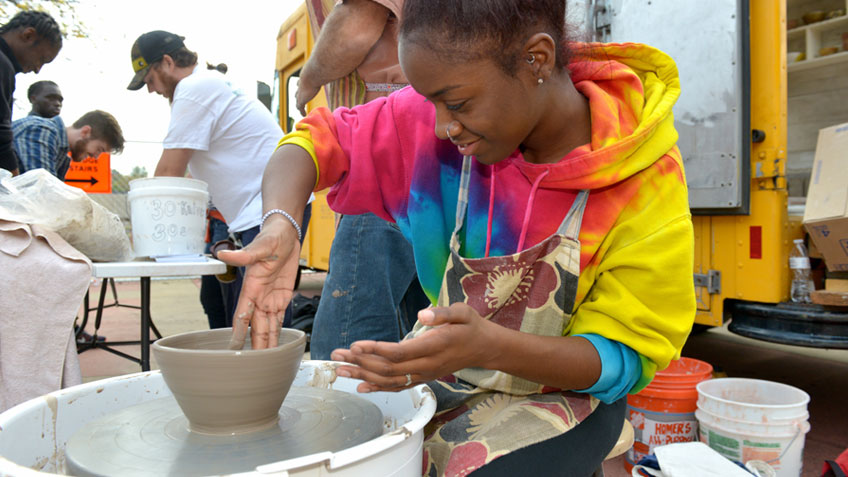 A smiling student creates a bowl using a pottery wheel