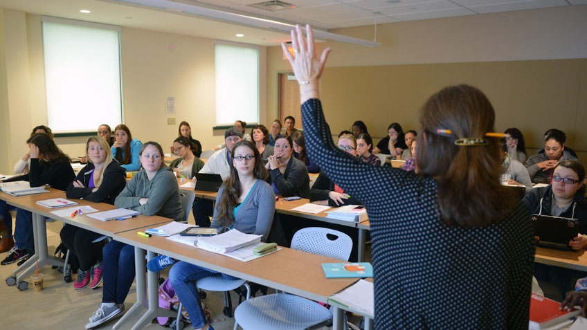 A teacher raising her hand before a classroom full of students