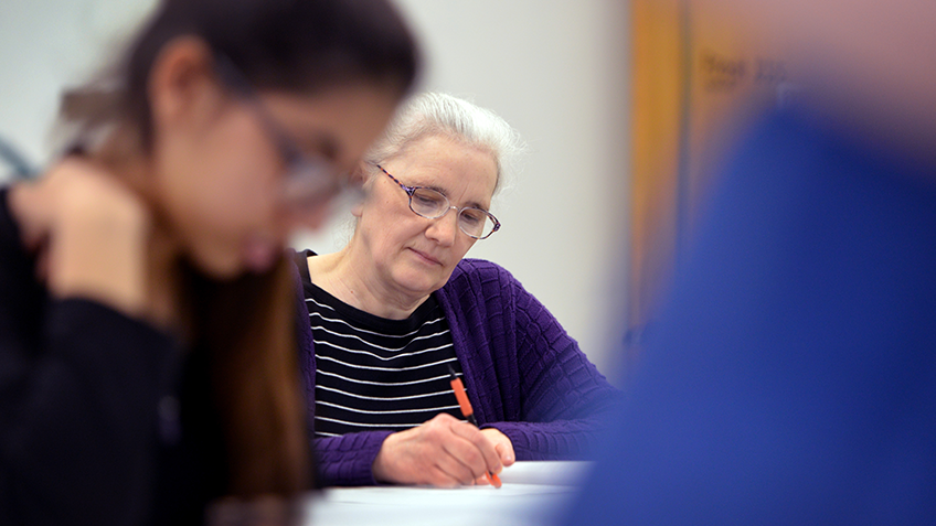 An adult student with white hair is in a classroom, working at a desk.